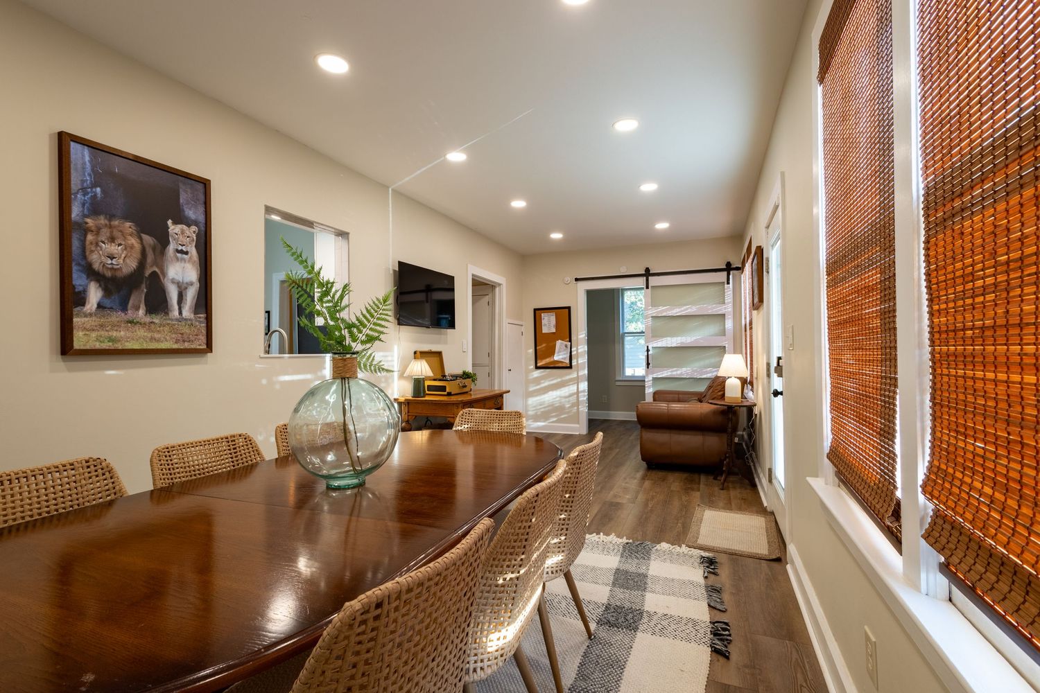 Spacious dining room with large wood table, barn door, recessed lighting, and bamboo window shades.