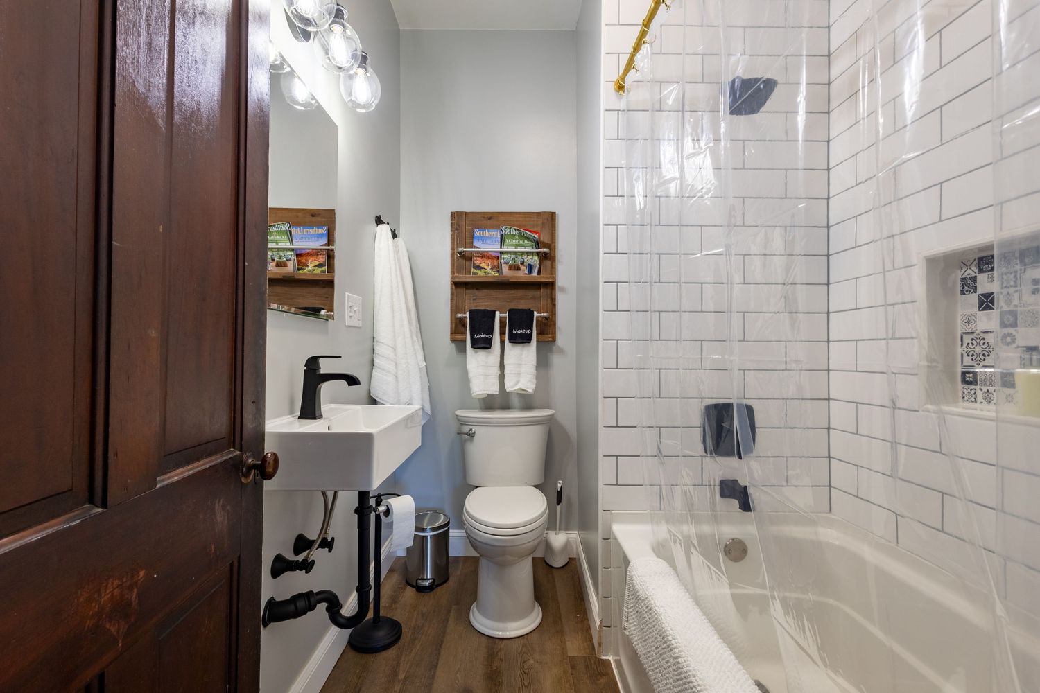 Compact bathroom with white subway tile shower, pedestal sink, toilet, and dark hardwood flooring.