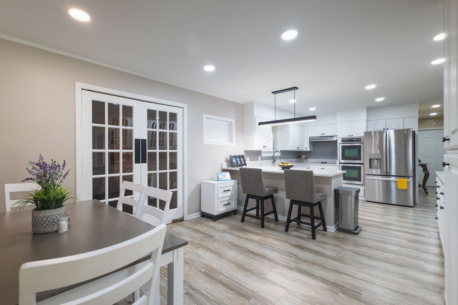 Bright open kitchen with white cabinets, gray island, stainless steel appliances, and French doors.