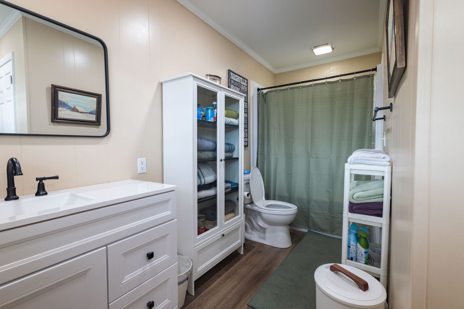 Clean bathroom with white vanity, black faucet, storage cabinet, and green shower curtain.