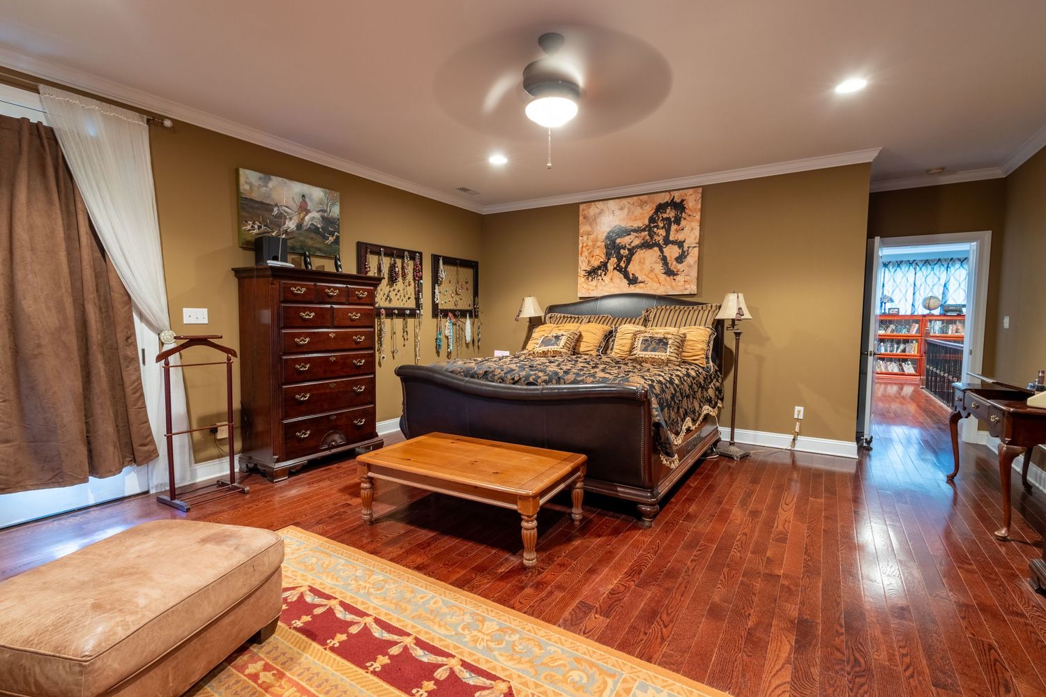 Large master bedroom with hardwood floors, decorative horse artwork, ceiling fan, and bench at foot of bed.