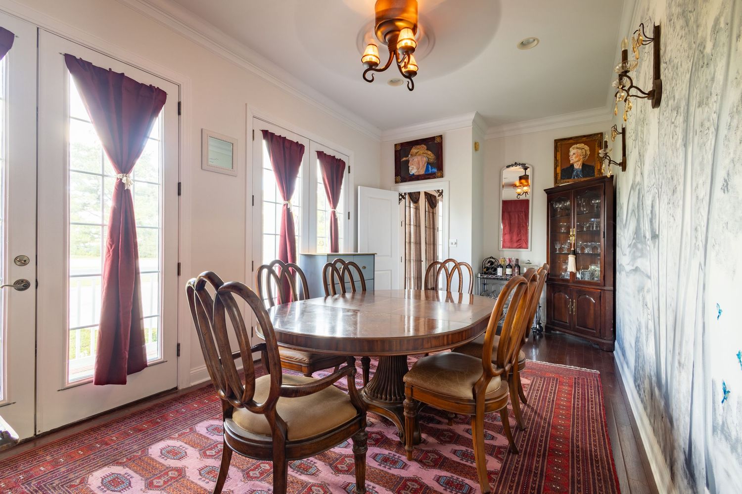 Formal dining room with oval wooden table, upholstered chairs, ornate chandelier, and decorative wallpaper.