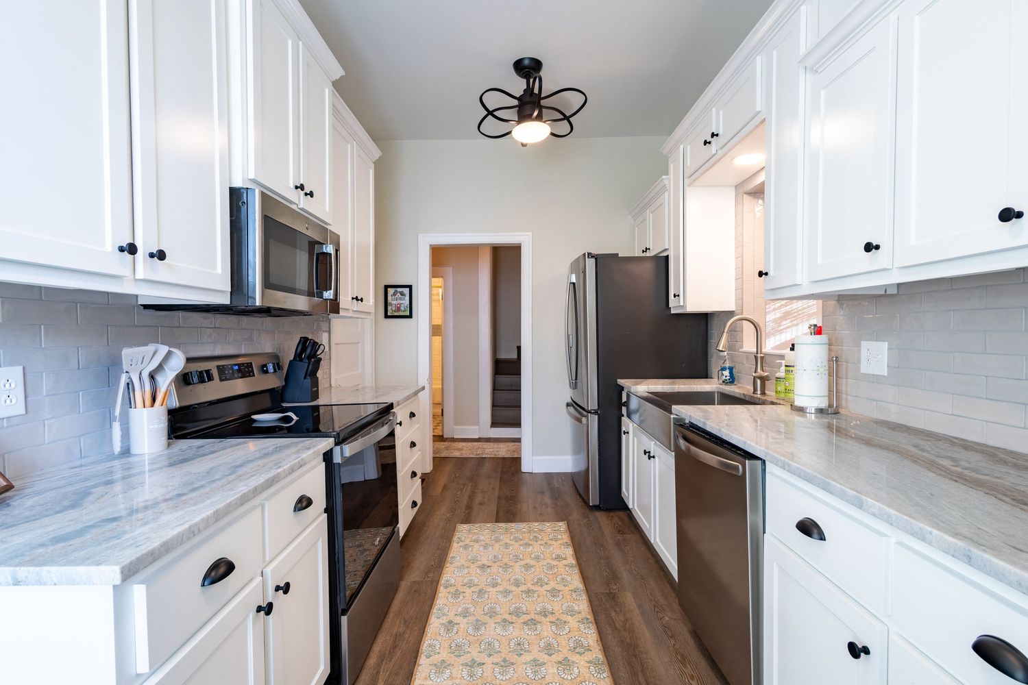 Galley kitchen with white cabinets, marble countertops, and stainless steel appliances.