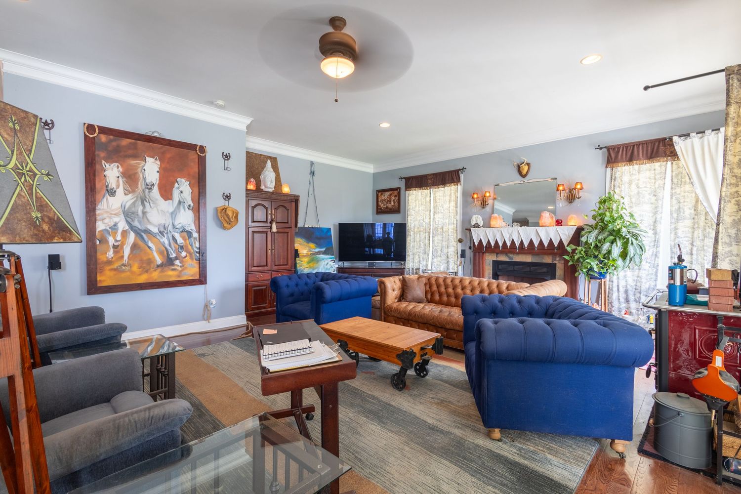 Eclectic living room with blue velvet sofas, leather chair, and decorative wall art.