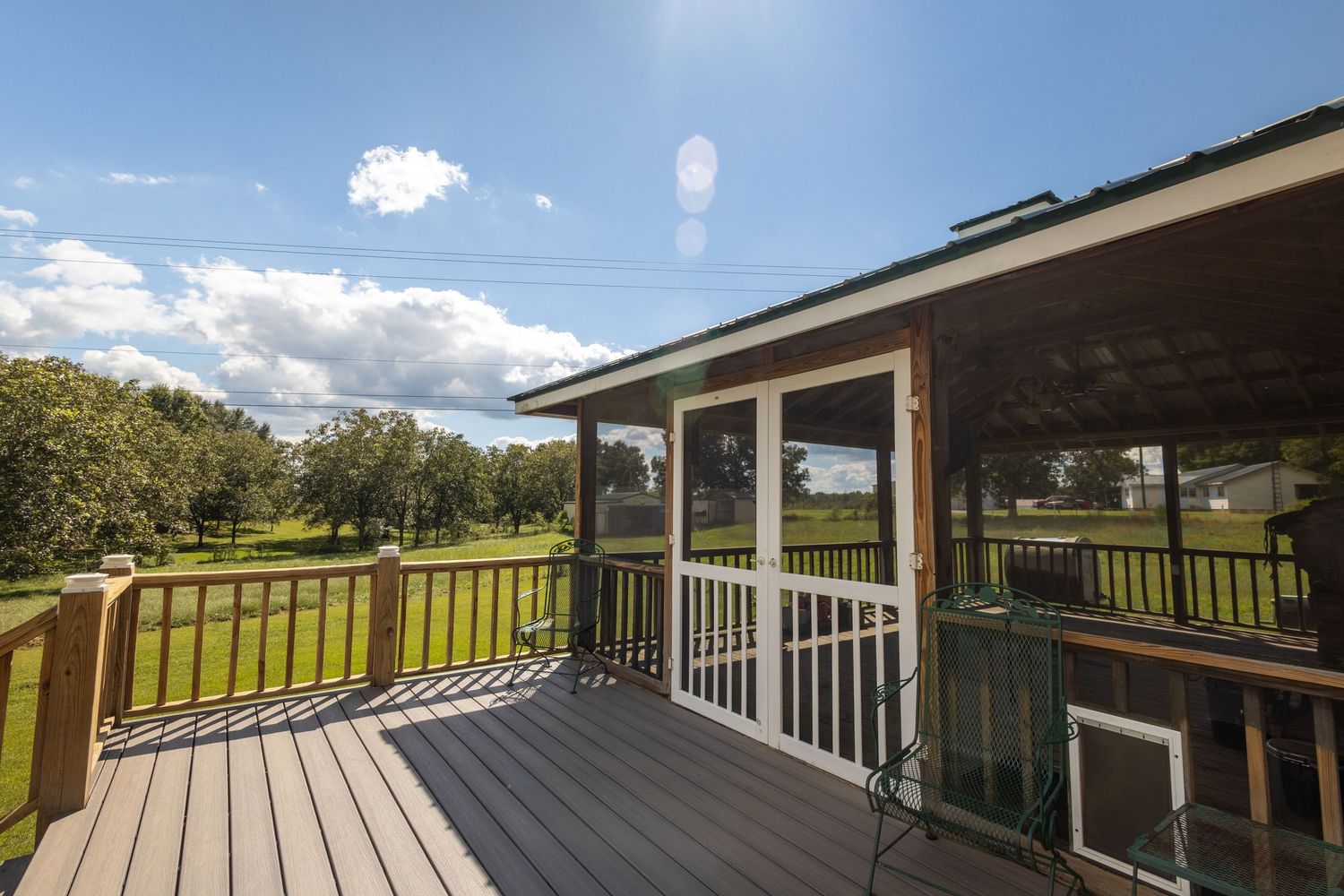 Wooden deck with screened porch attached, overlooking lush green lawn under bright sunny sky.