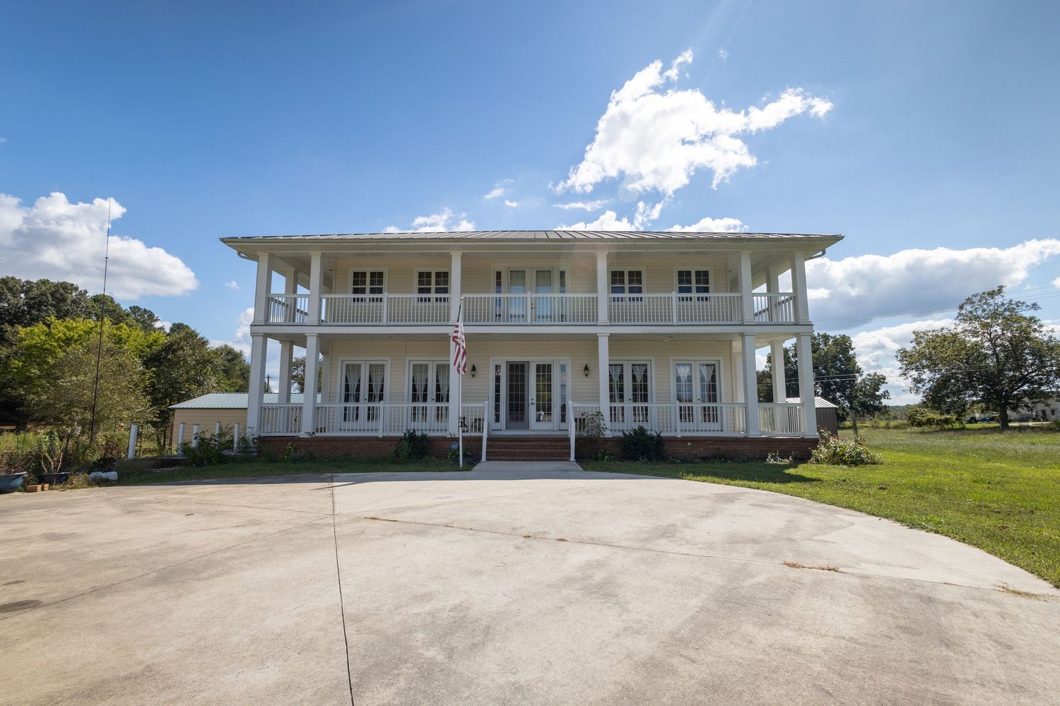Large two-story white plantation-style home with wraparound balcony, columns, and spacious driveway.