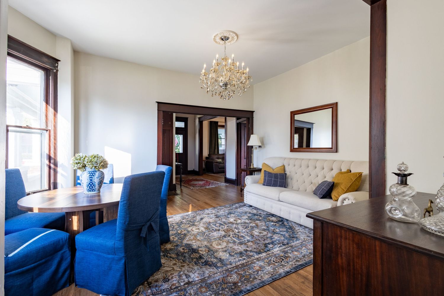 Cozy living room with tufted sofa, blue accent chairs, crystal chandelier, and hardwood floors.