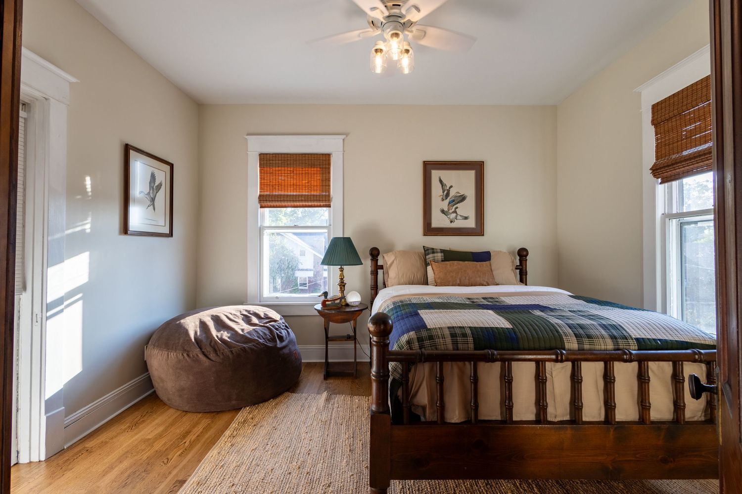 Cozy bedroom with hardwood floors, plaid bedding, bean bag chair, and bamboo shades on windows.