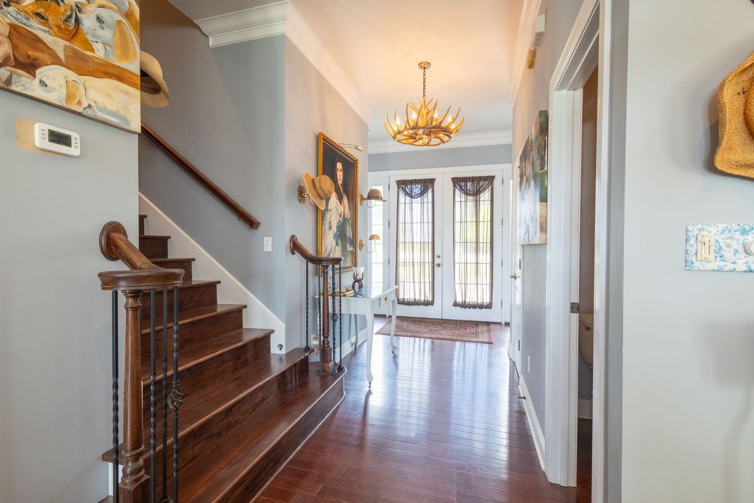 Elegant foyer with dark hardwood floors, grand staircase, chandelier, and glass-paneled front door.
