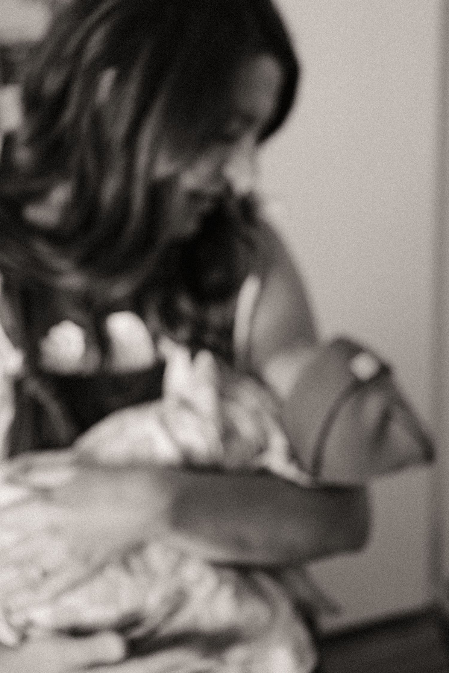 Black and white photo of a smiling woman with long wavy hair gently cradling a swaddled newborn baby in her arms.