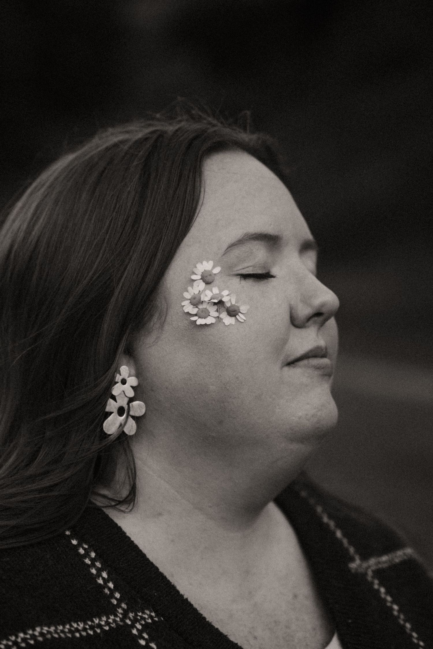 Black and white profile portrait of a woman with closed eyes, daisy stickers on her cheek, and matching flower earrings.