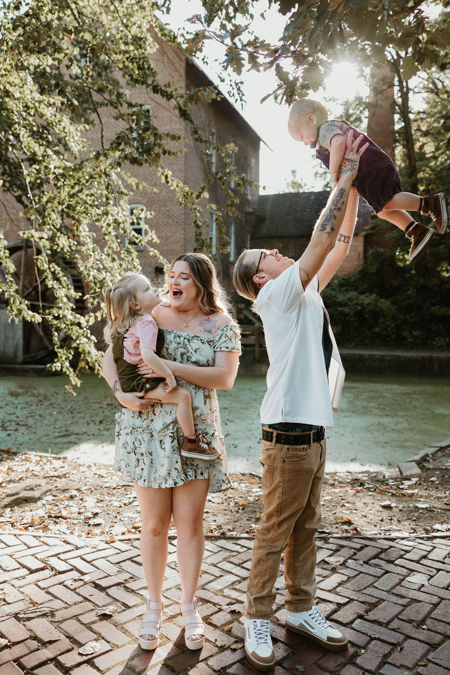 Happy family with two young children playing outdoors near a brick building in golden sunlight.