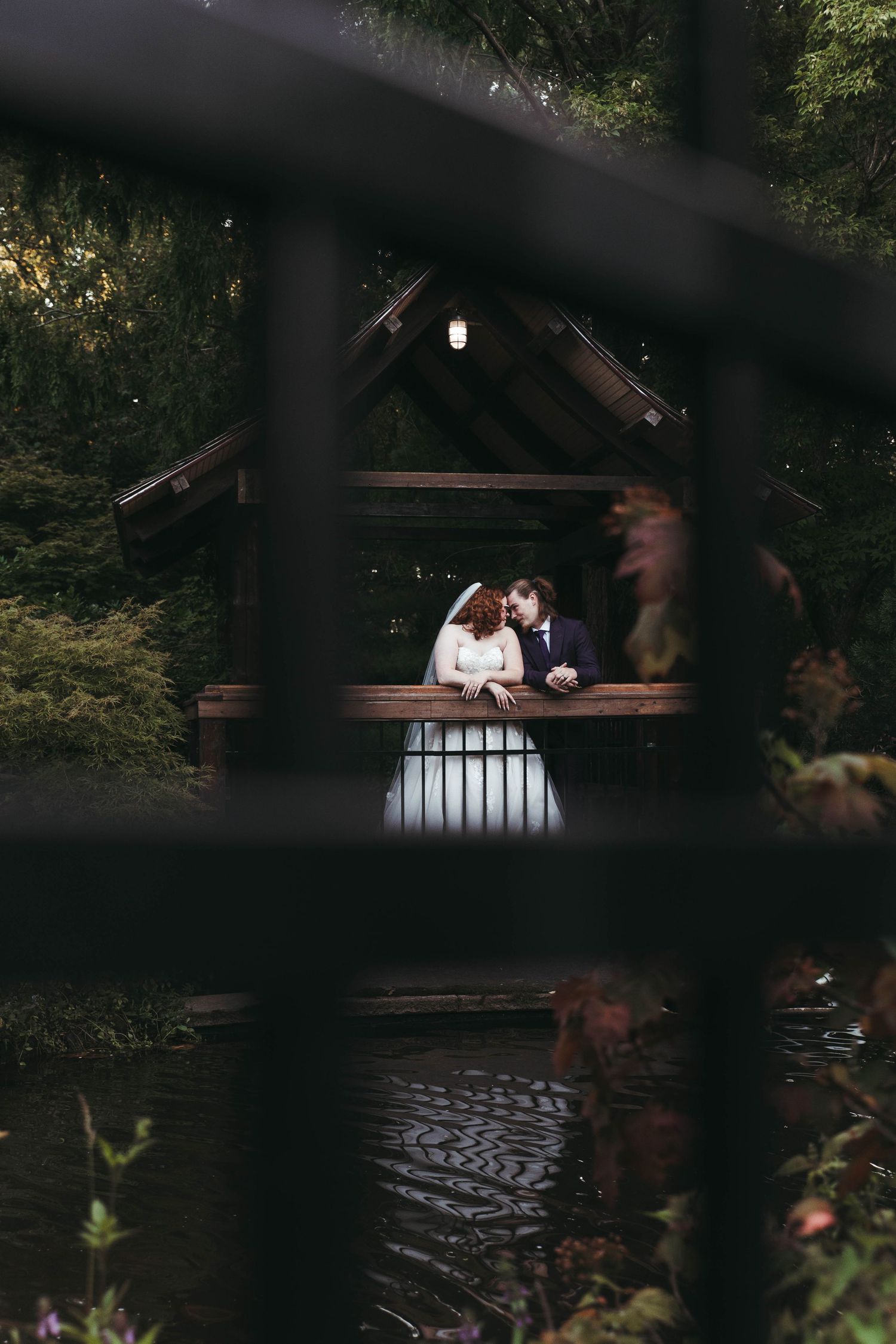 Bride and groom sharing an intimate moment in a wooden gazebo overlooking a tranquil pond.
