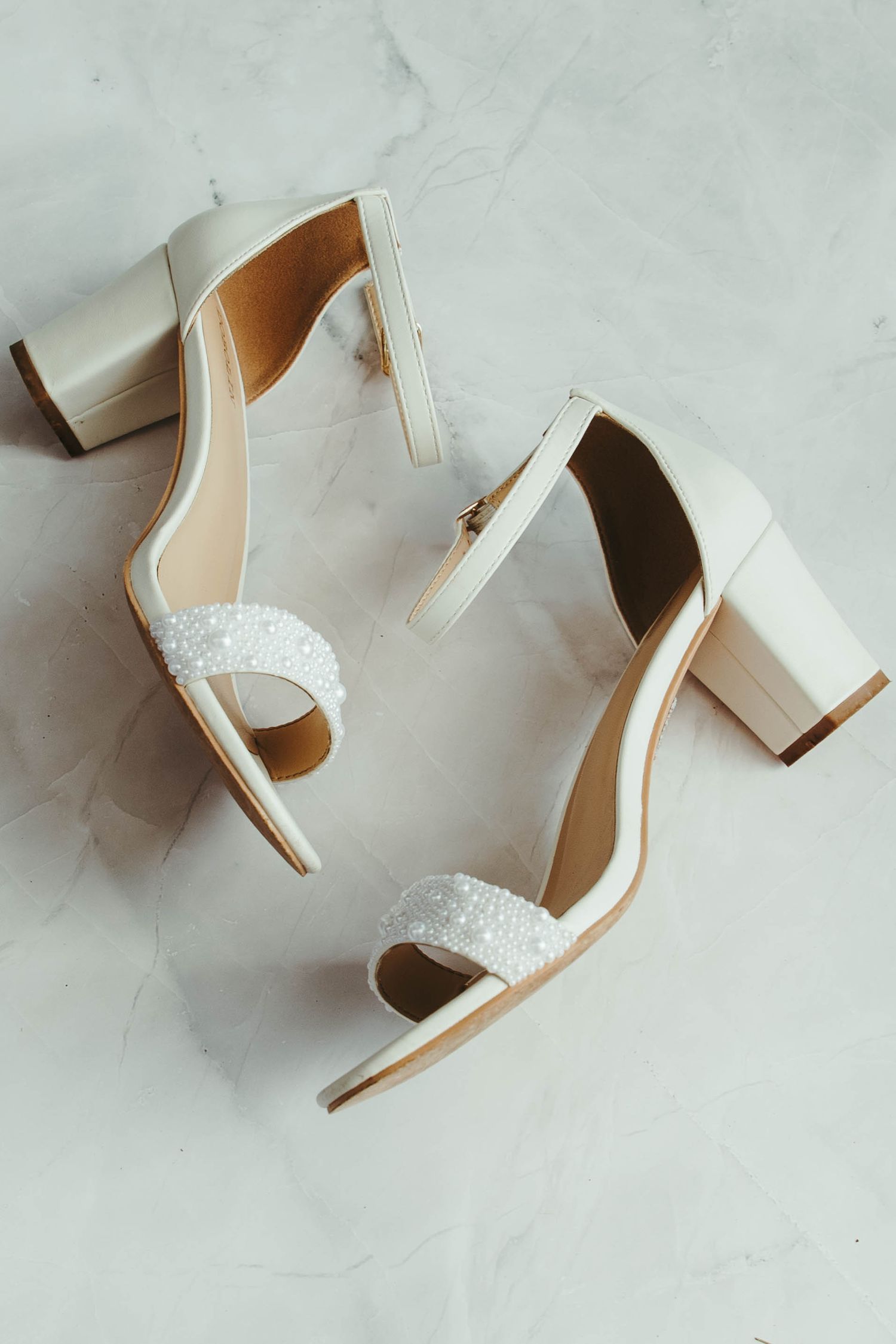 White block heel sandals with pearl embellished toe strap on marble surface.