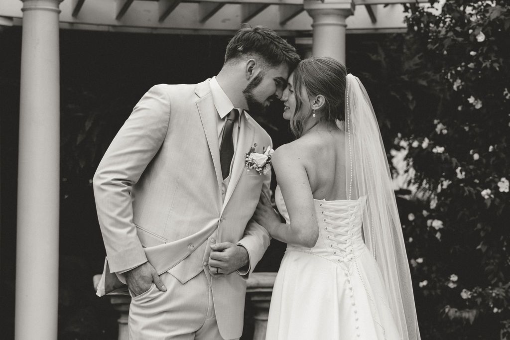 Black and white wedding photo of bride and groom sharing an intimate moment, touching foreheads outdoors.