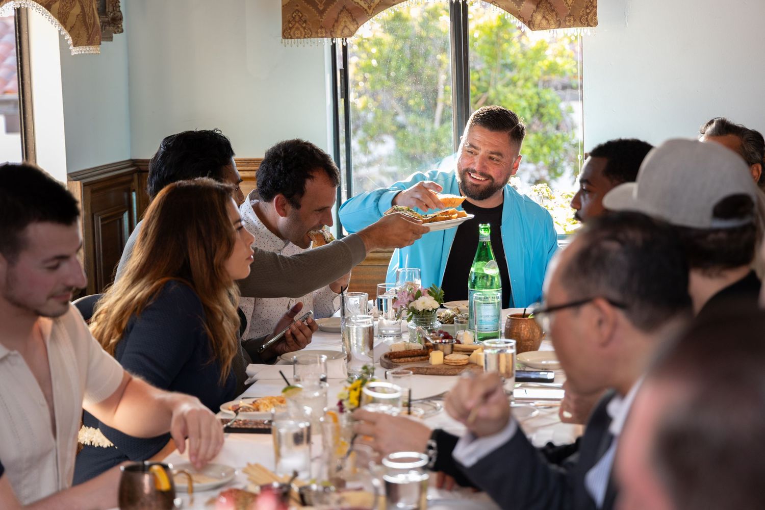Diverse group of people sharing food at restaurant table during lively social gathering.