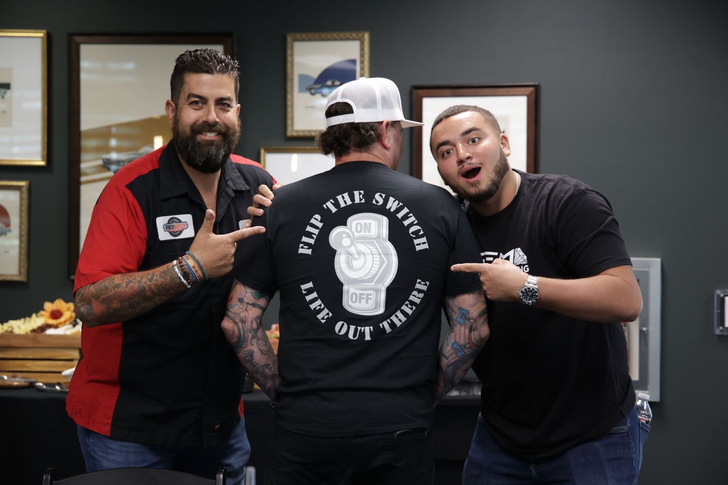 Three men smiling and posing with Flip The Switch t-shirt inside a tattoo shop.