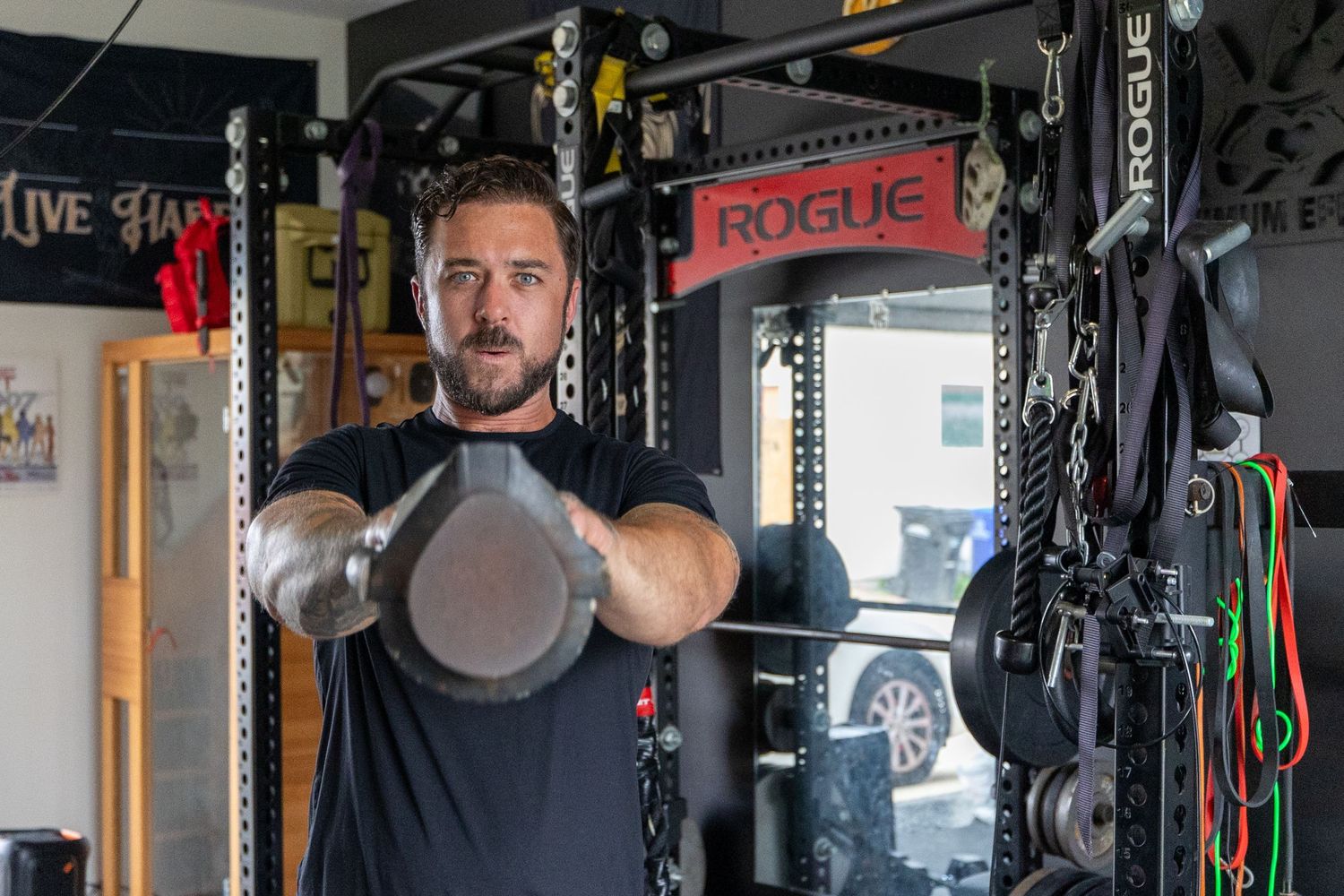 Man lifting kettlebells in home gym with Rogue equipment.