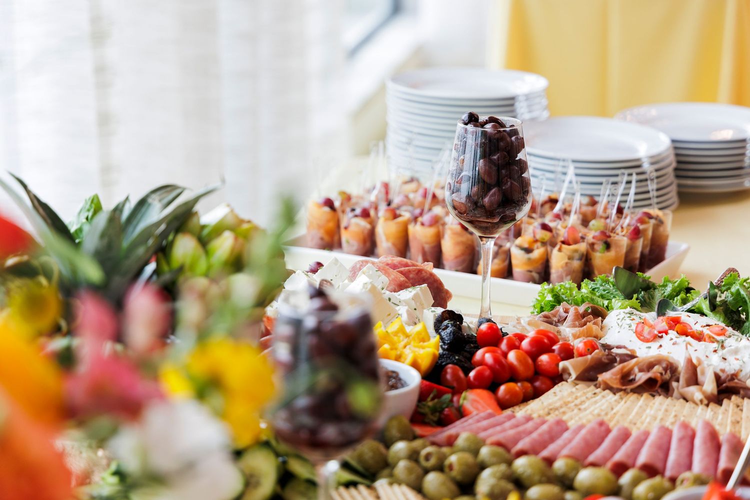 Elegant catering spread with charcuterie, olives, tomatoes, and appetizers on a table.