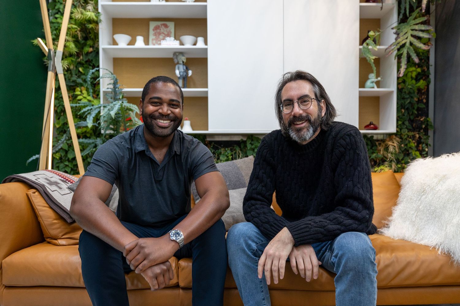 Two men smiling together on leather couch in modern studio.