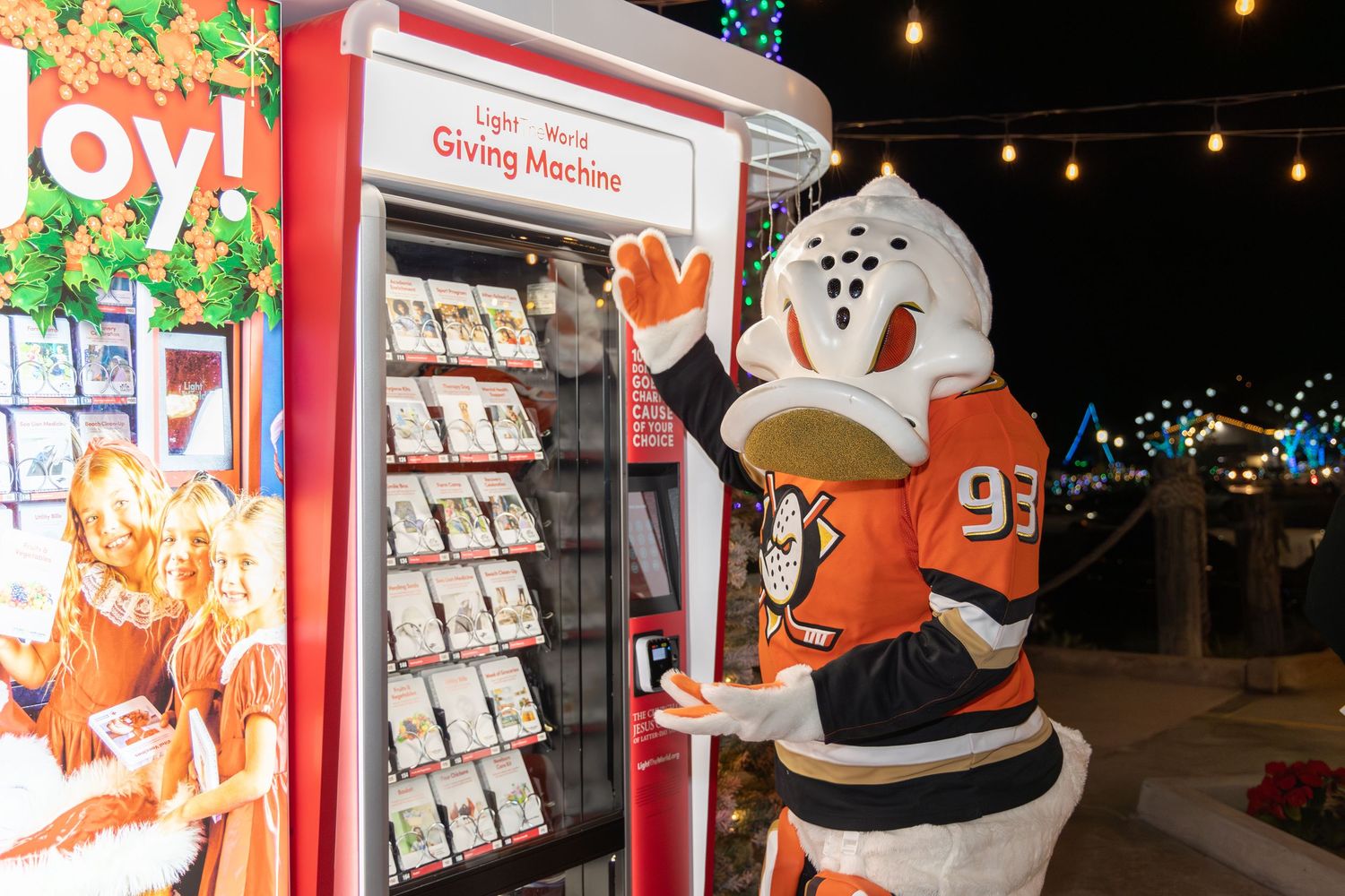 Anaheim Ducks mascot Wild Wing waving next to a holiday Giving Machine vending display.