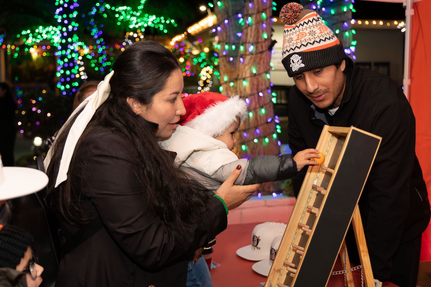 Family with baby exploring a holiday light display at an outdoor Christmas event.