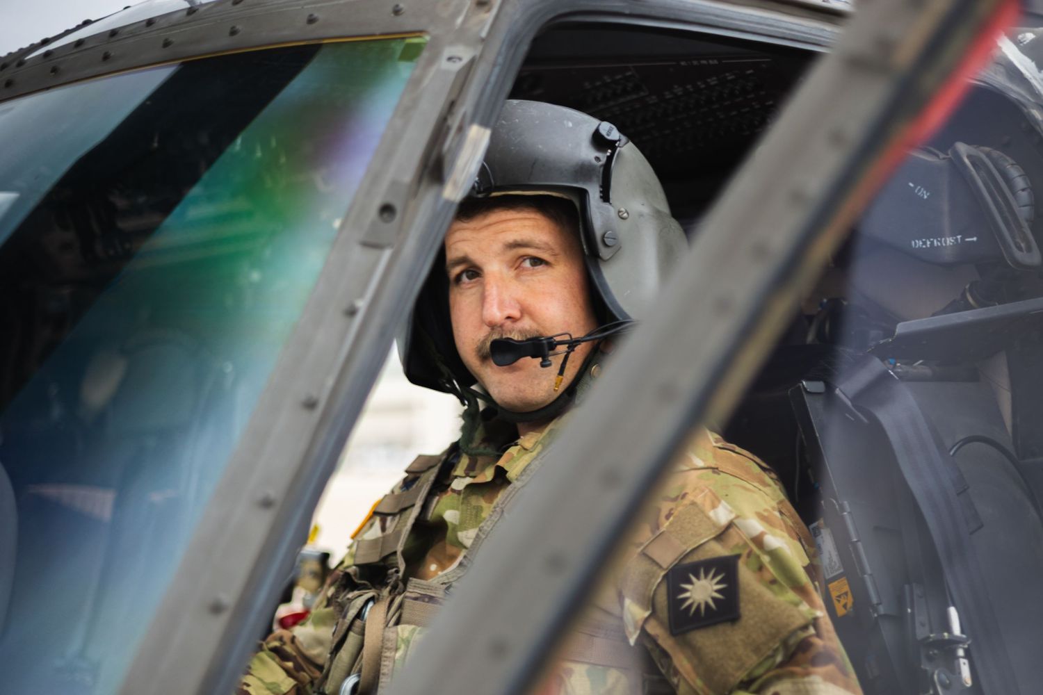 Military helicopter pilot in cockpit wearing flight helmet and tactical gear.