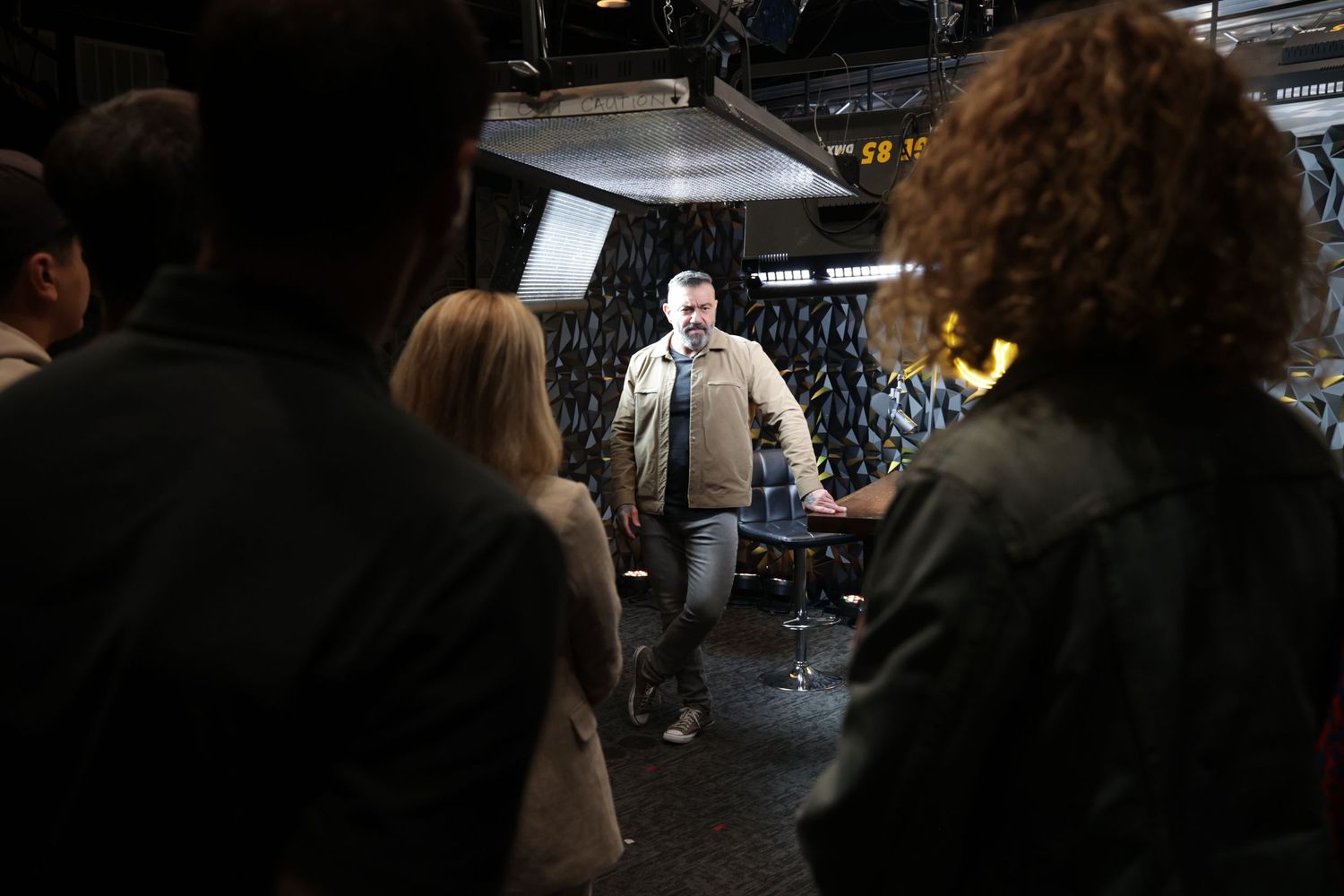 Man presenting to a group of people on a dimly lit film or TV set.