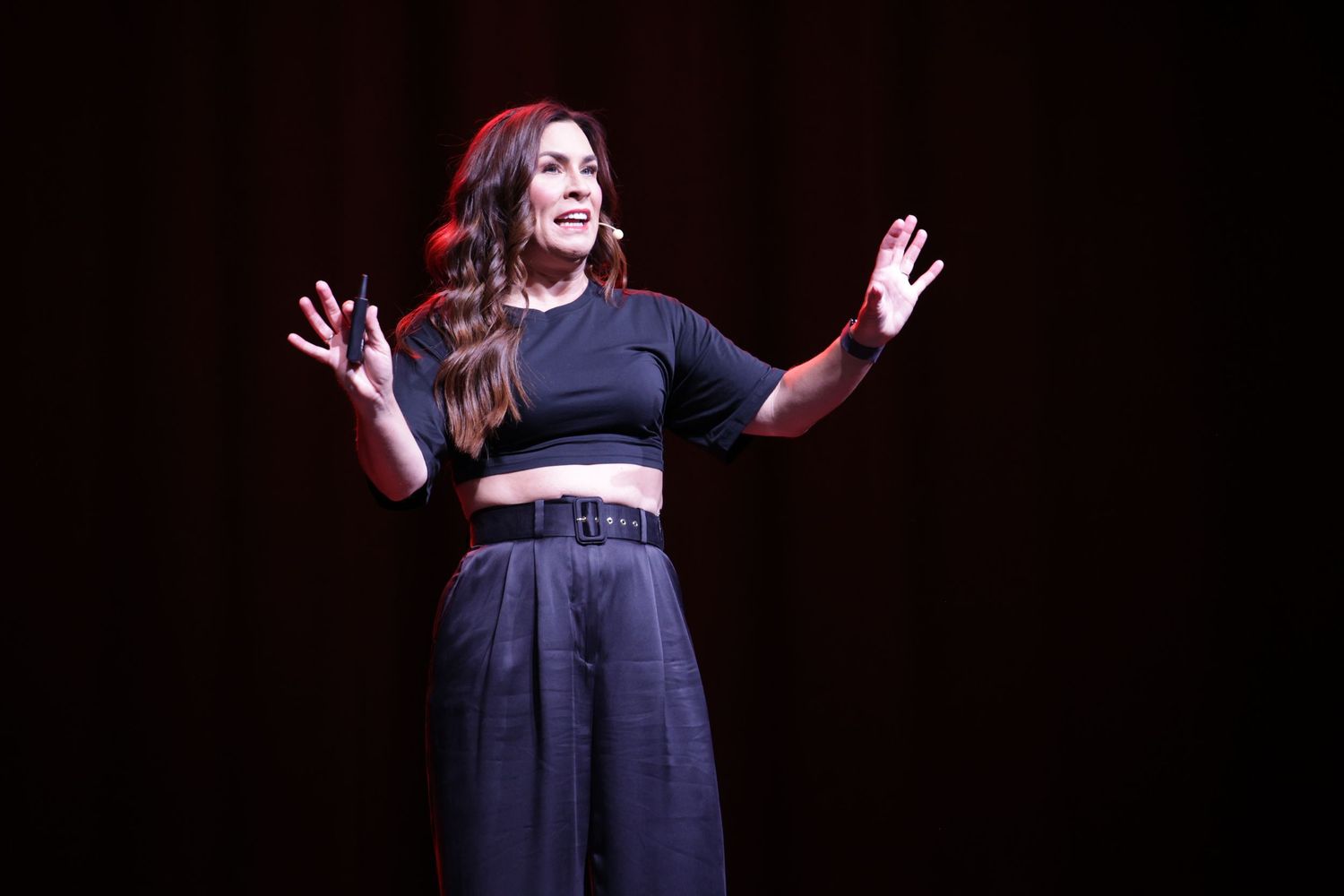 Woman in black crop top and wide-leg pants performing on a dark stage.