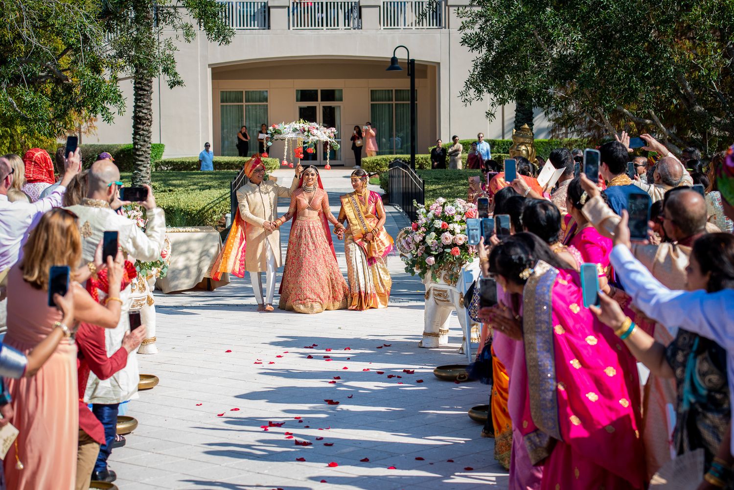 Wedding procession with attendees in colorful attire walking down decorated aisle.