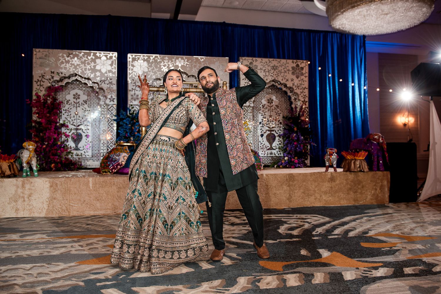 Wedding couple dancing joyfully on patterned floor in front of decorative backdrop at reception.