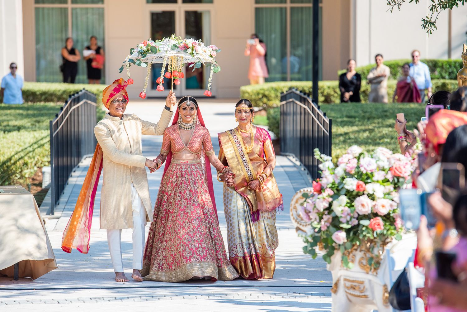 Wedding ceremony setup outdoors with elaborate floral decorations and traditional Indian outfits.