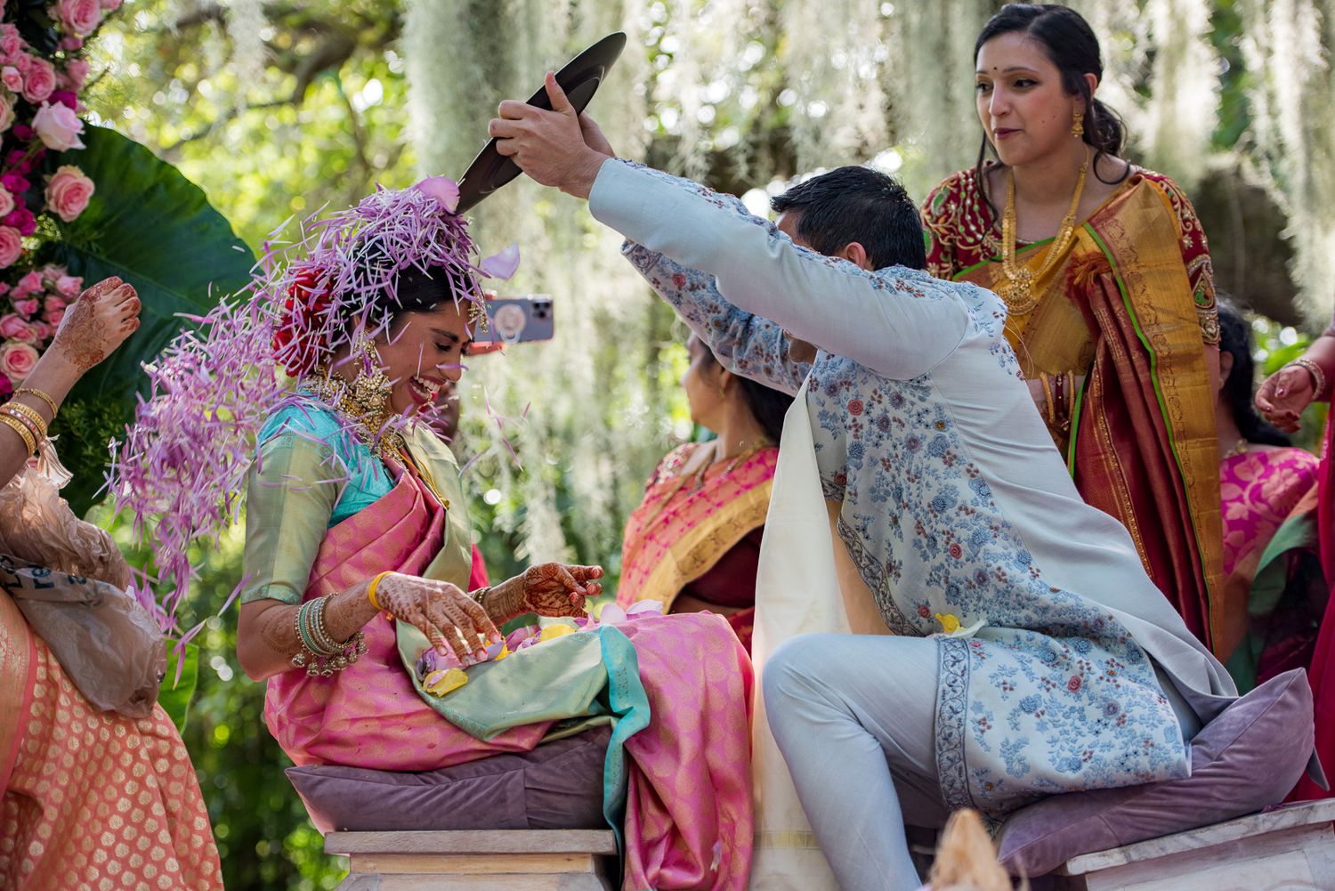 Traditional Indian wedding ceremony showing playful moments during ritual celebrations in an outdoor garden setting.