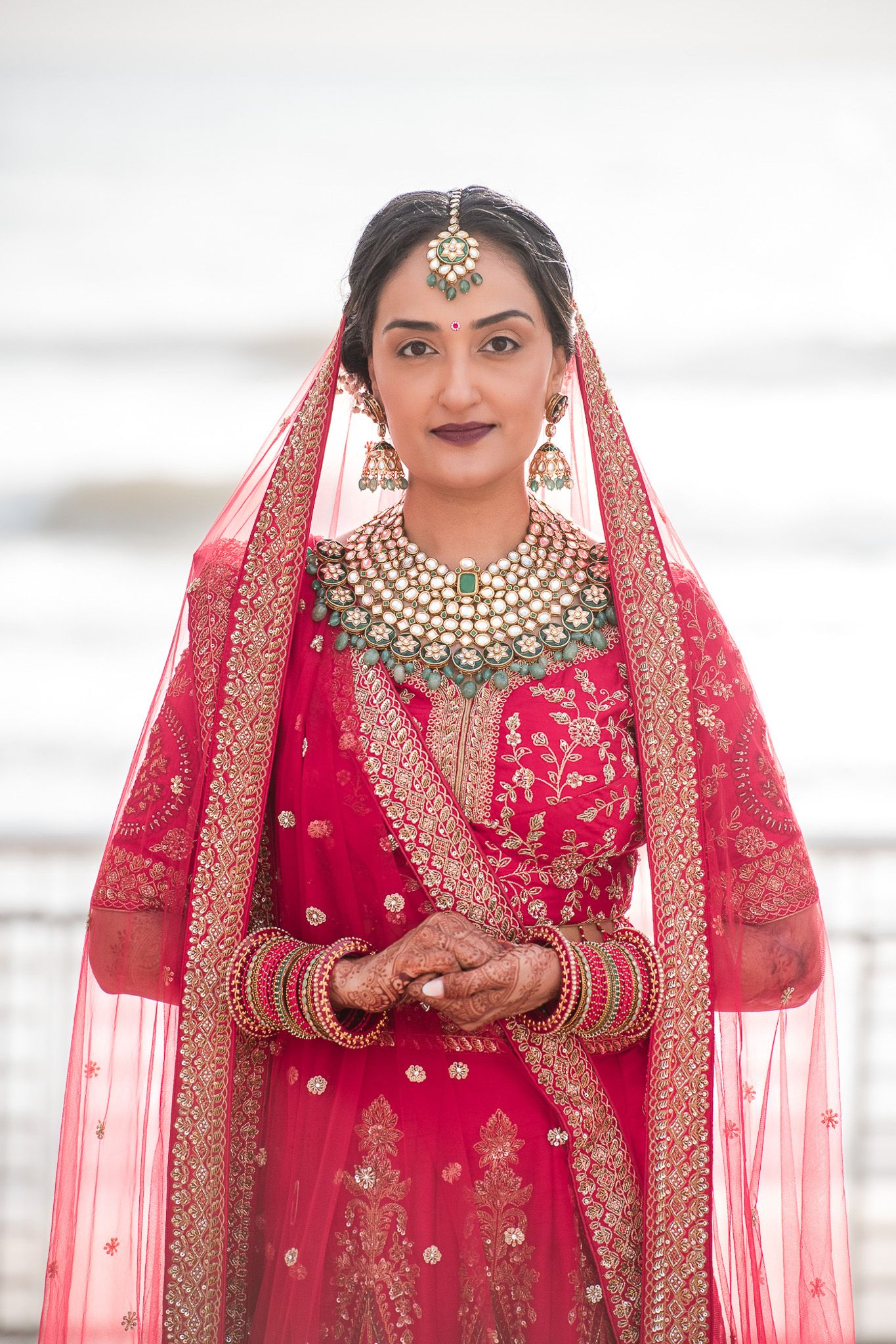 Bride wearing traditional red lehenga with ornate gold jewelry and headpiece in bridal portrait.