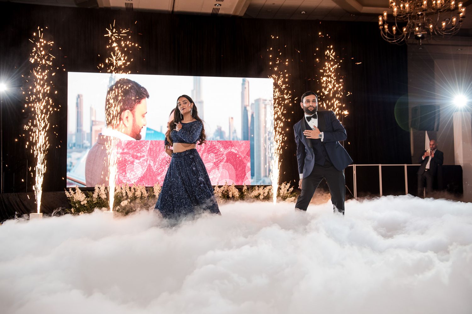 Performers dancing on stage with dramatic fog effects and sparkler fountains during special event.