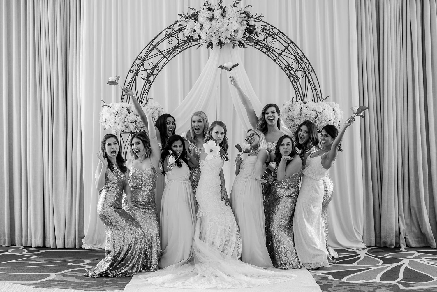 Wedding party poses under floral arch in celebration.