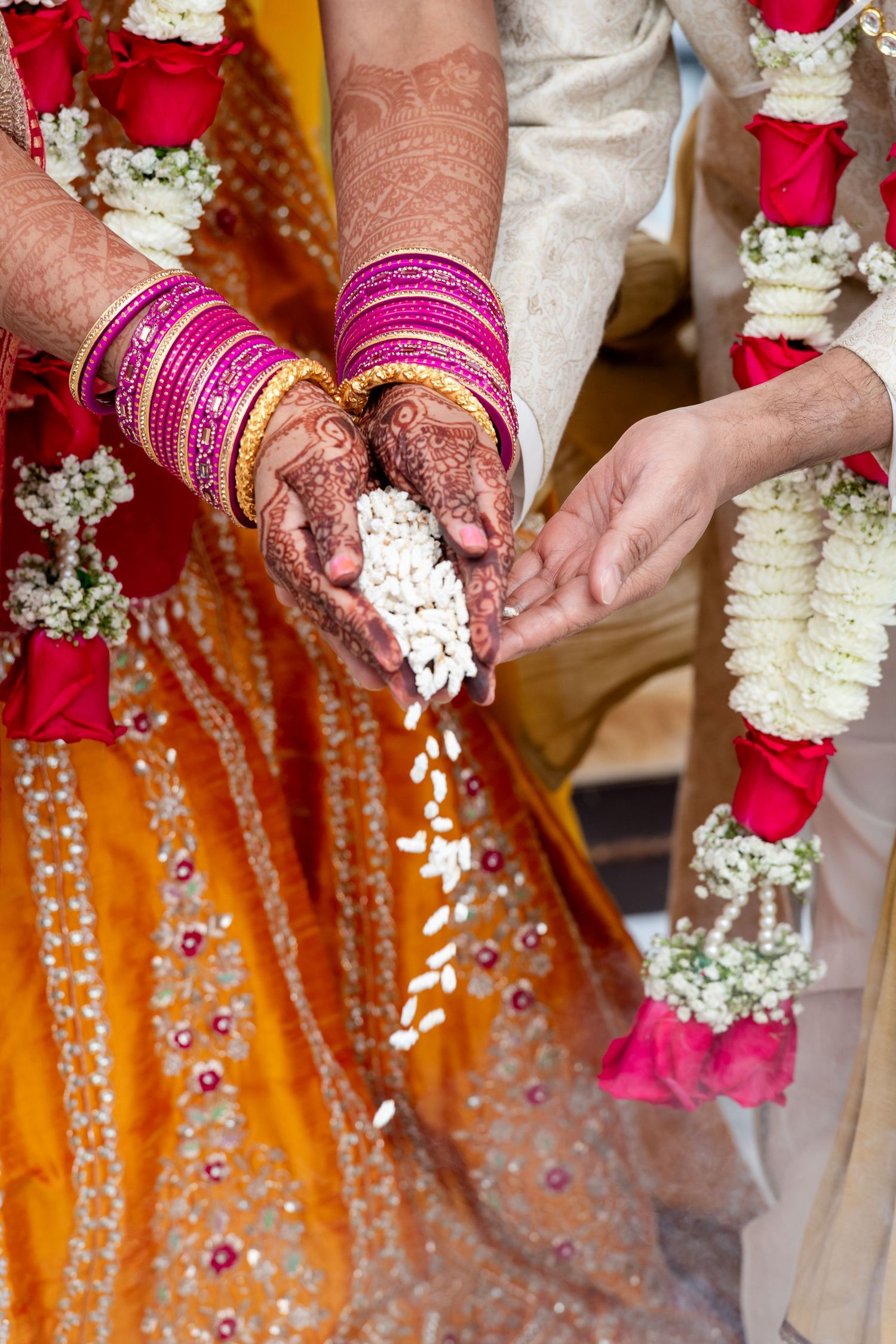 Close-up of hands with henna and pink bangles during traditional Indian wedding ceremony.