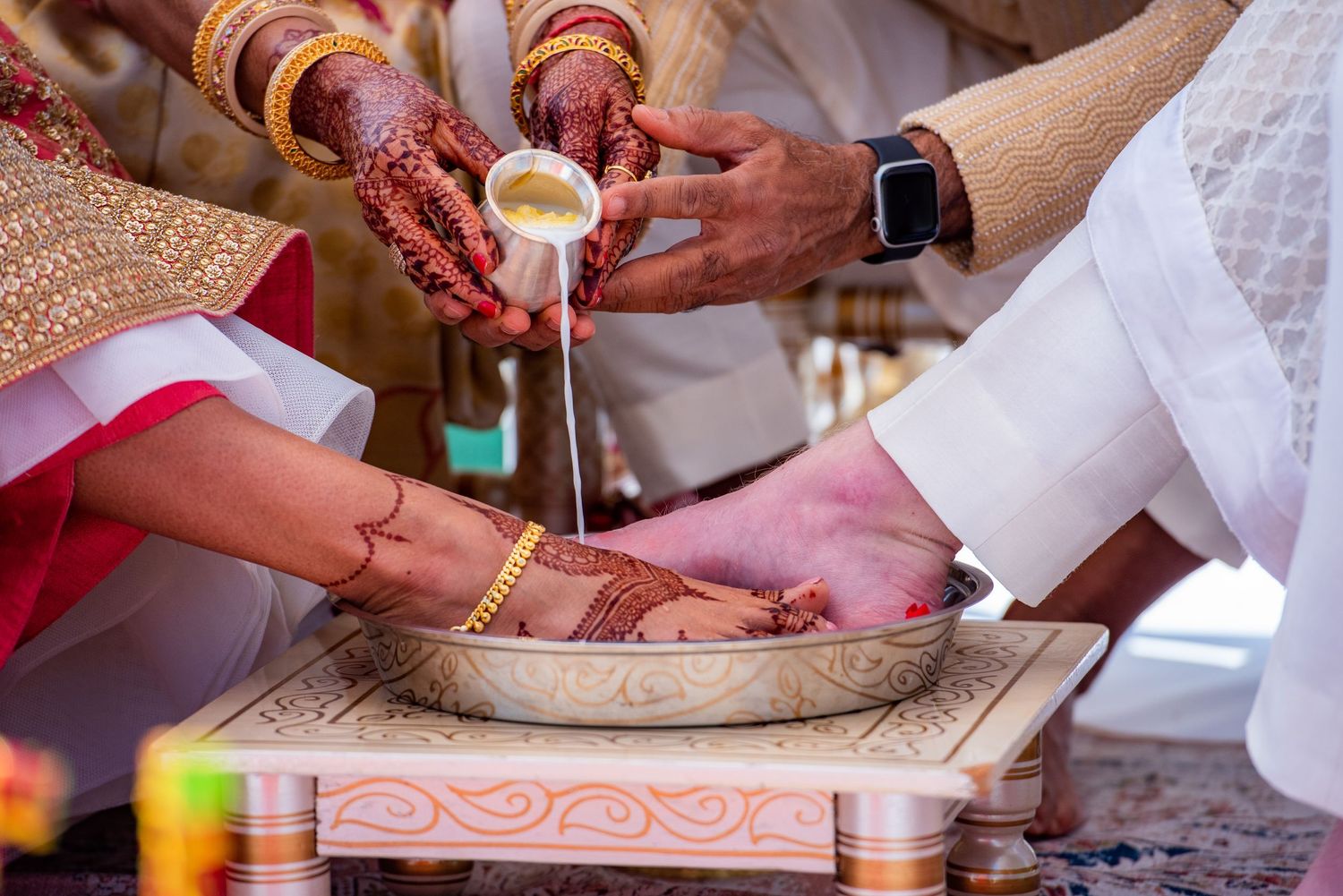 Close-up of hands performing traditional Indian wedding ritual with gold jewelry and ceremonial items.
