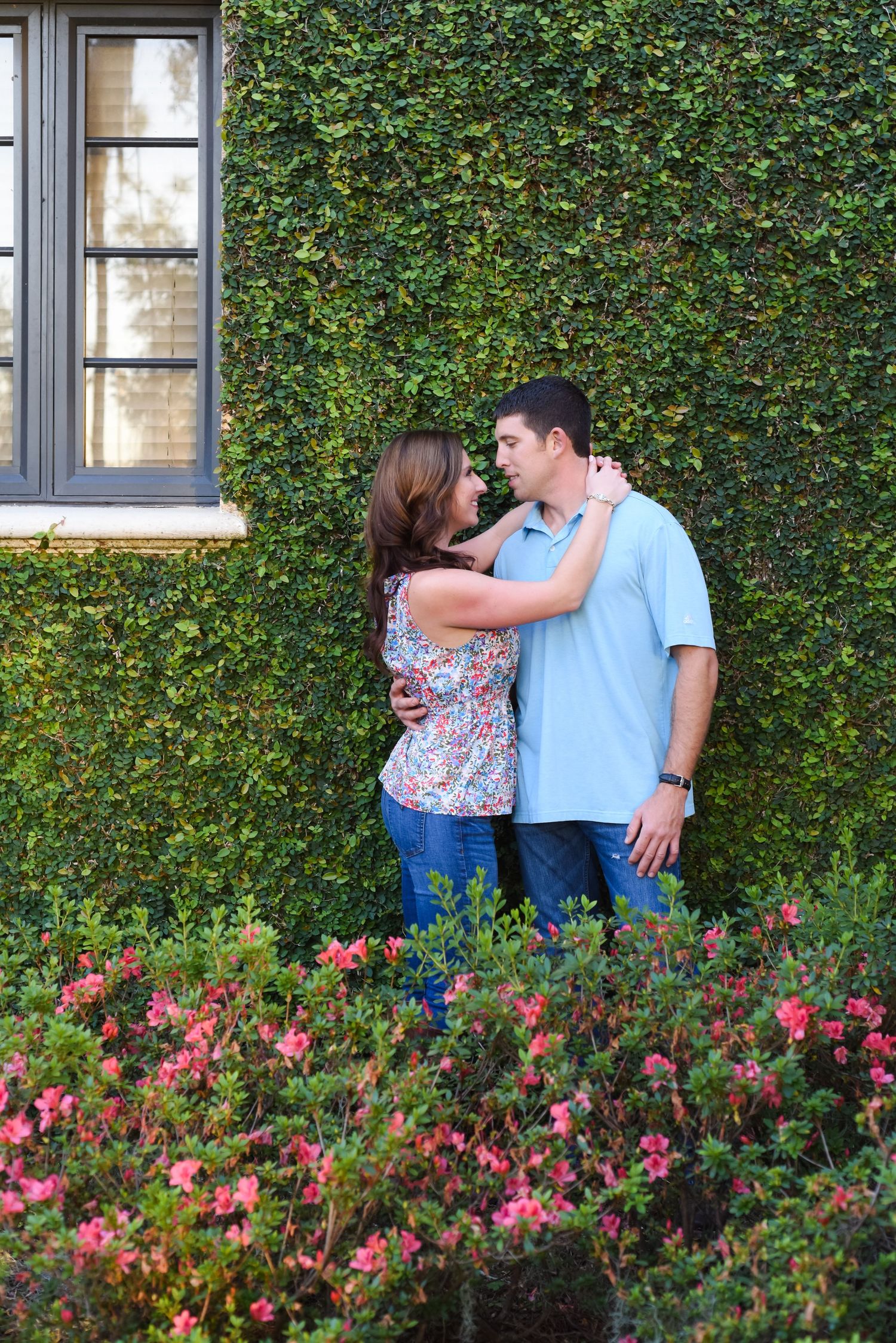 Romantic couple embracing against ivy covered wall with pink flowers in garden.