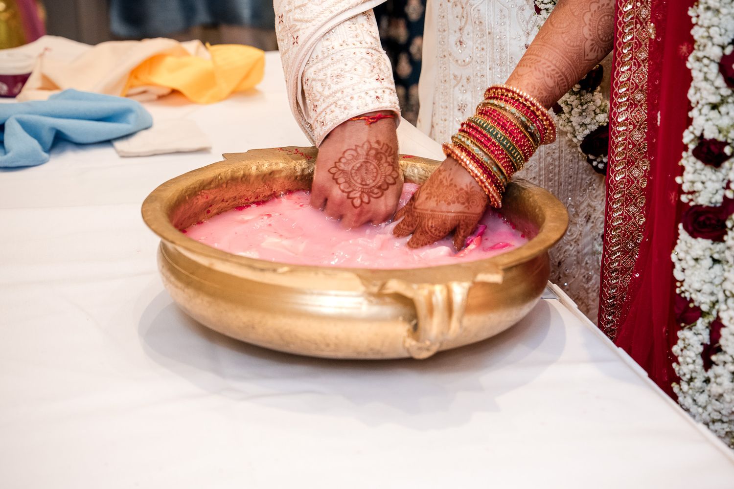 Close-up of hands performing a traditional Indian wedding ritual with pink powder in a golden bowl.