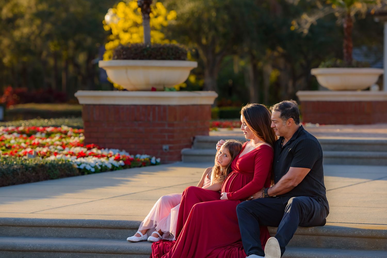 Family sitting together on stone steps in a garden with blooming flowers.