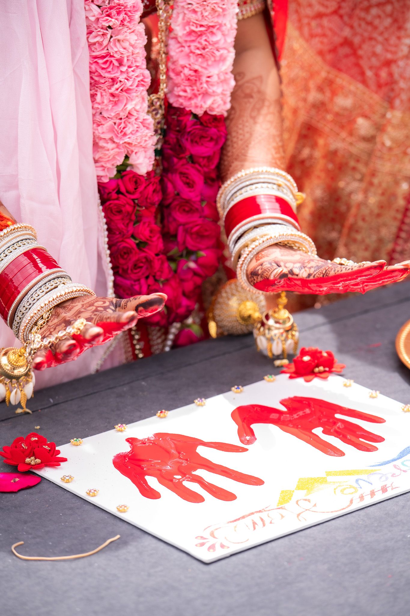 Traditional wedding ritual showing decorated hands and bangles with red handprints on white paper.
