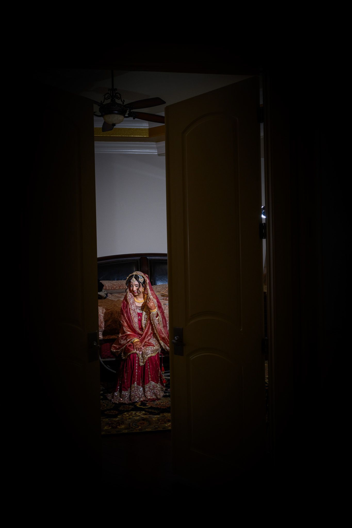Dramatic doorway shot revealing traditional bridal attire in dark moody lighting.