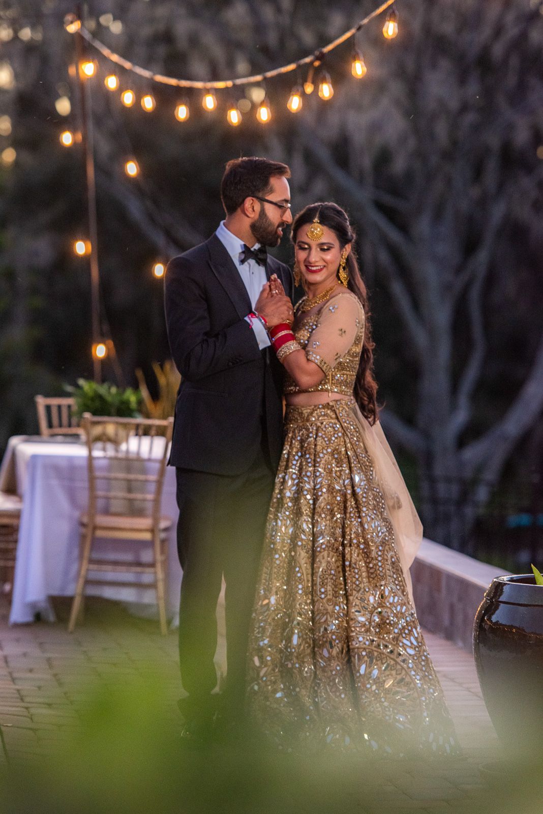 Romantic outdoor evening reception with string lights and a couple in traditional Indian fusion attire.