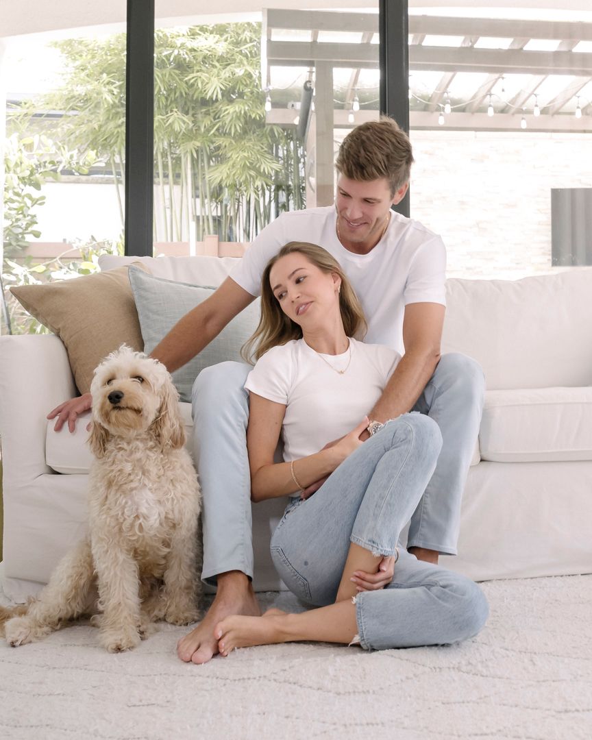 Couple and their goldendoodle dog lounging together on white couch in bright modern room.