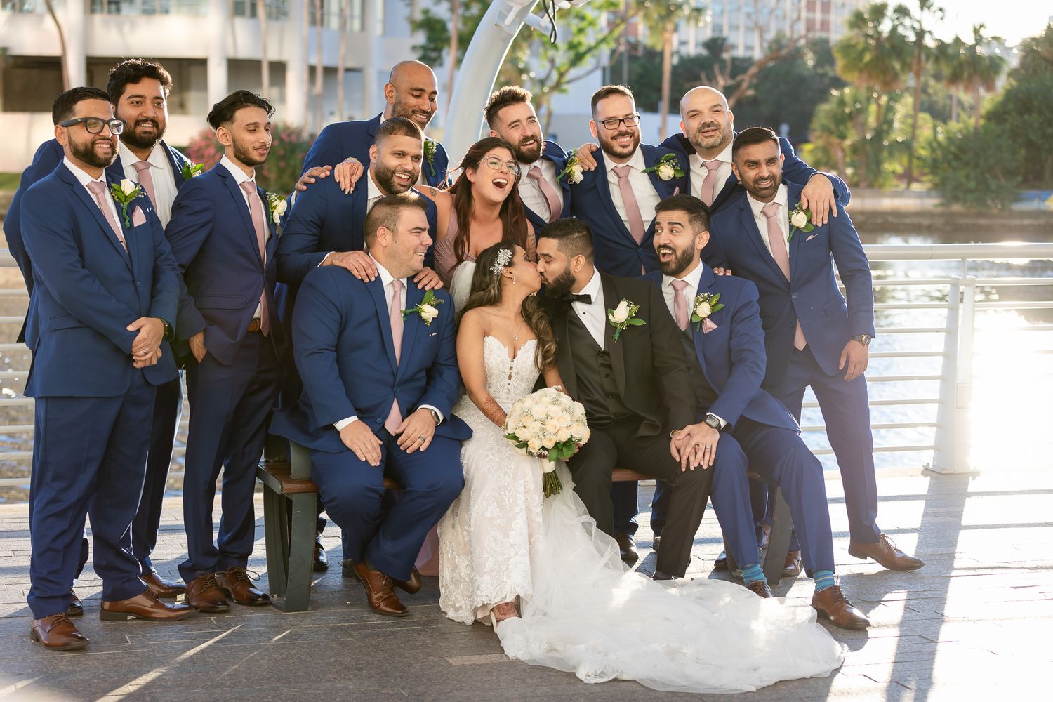 A wedding party in navy suits and formal attire poses together outdoors.