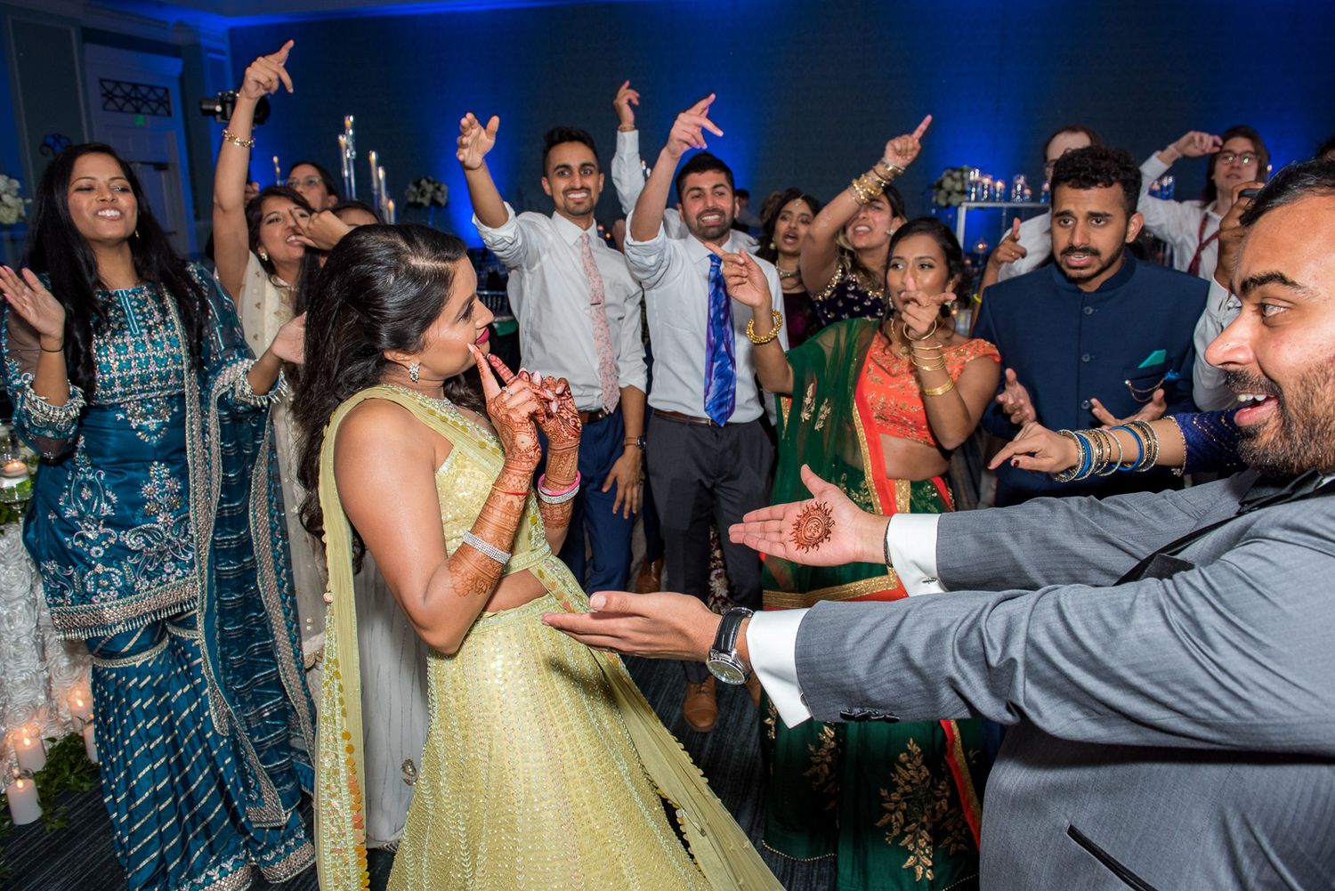 Energetic dance celebration at an Indian wedding reception with guests in formal attire.