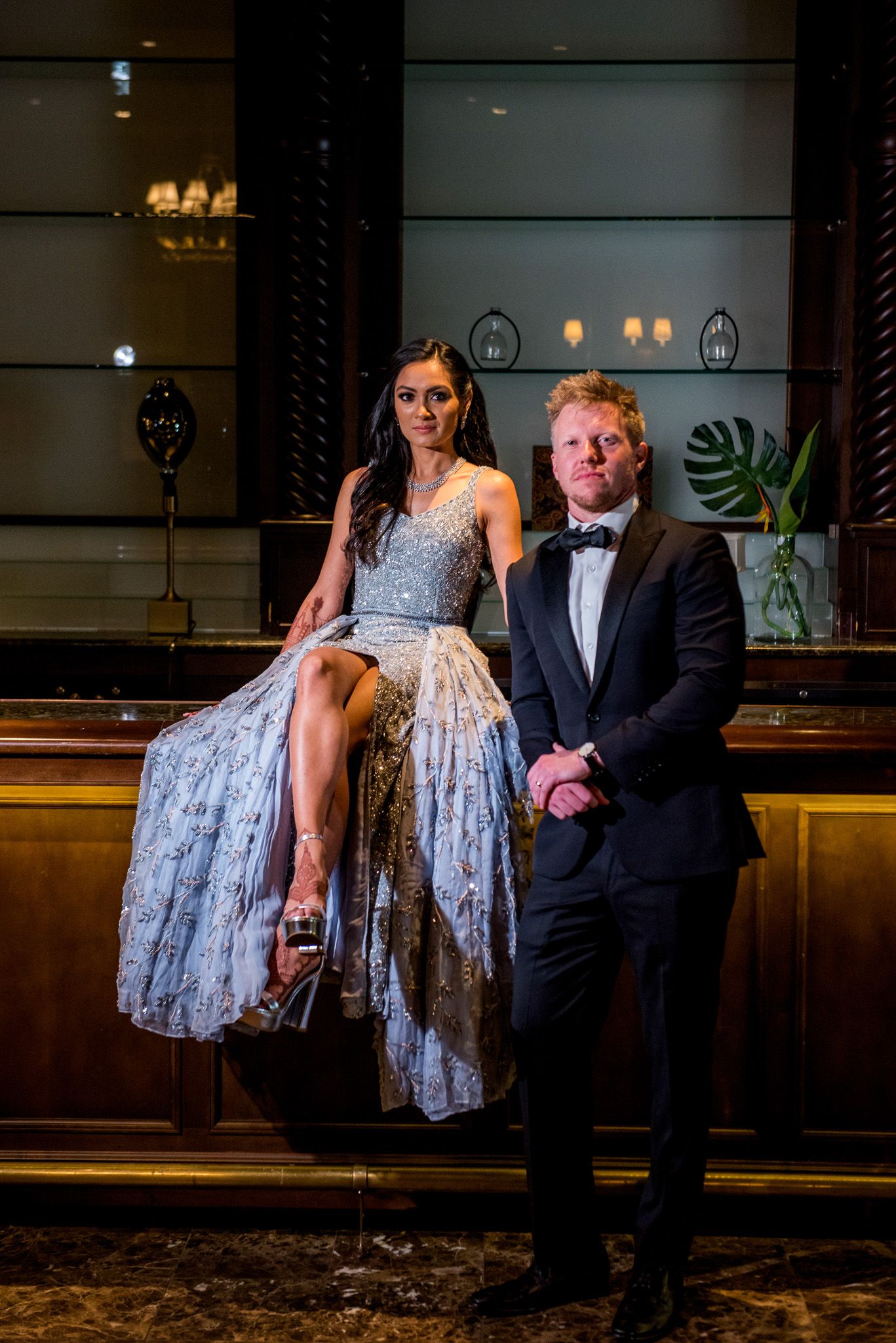 Glamorous couple poses at an elegant bar with mood lighting and modern decor.