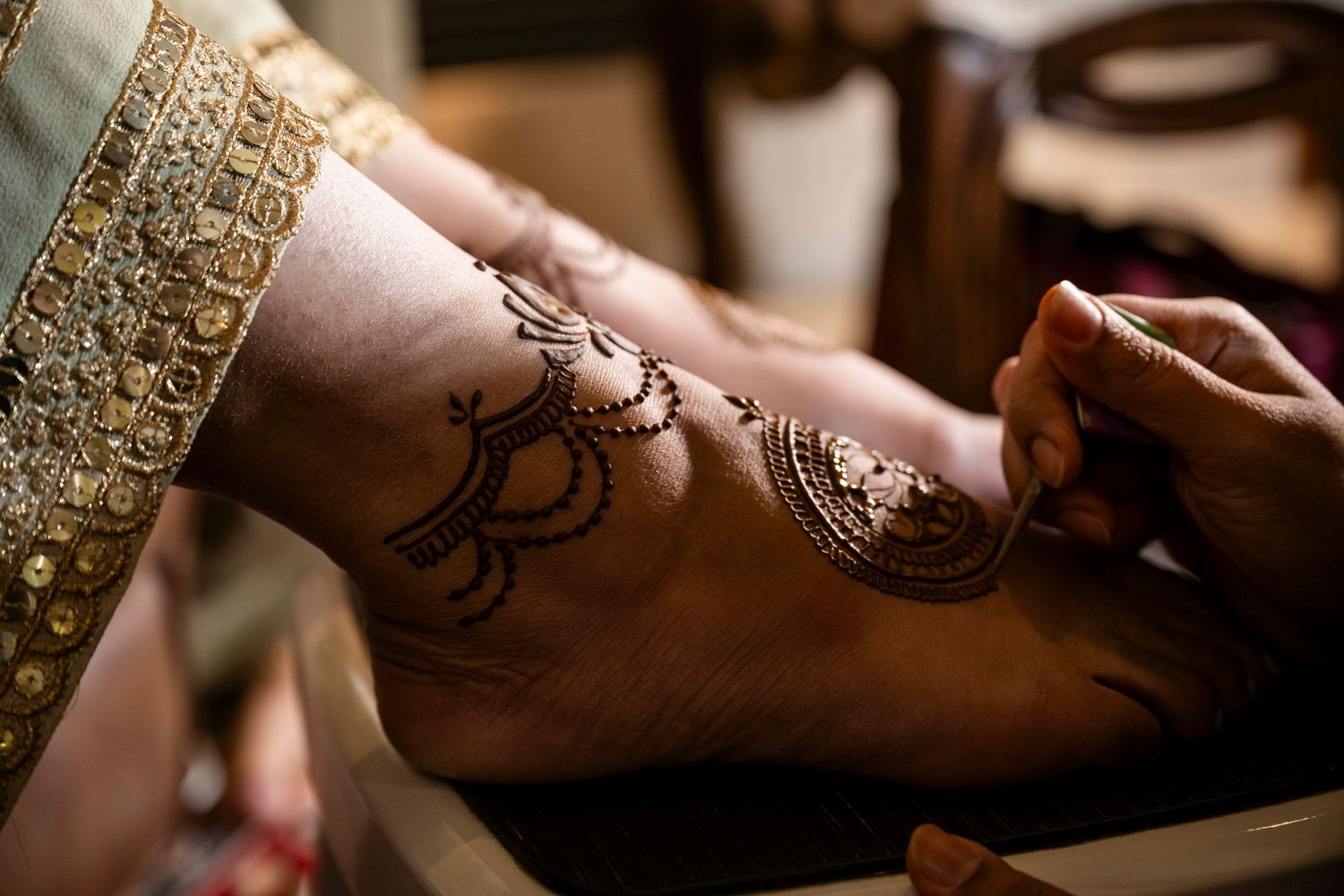 Close-up of intricate henna design being applied to someone's foot during wedding preparations.