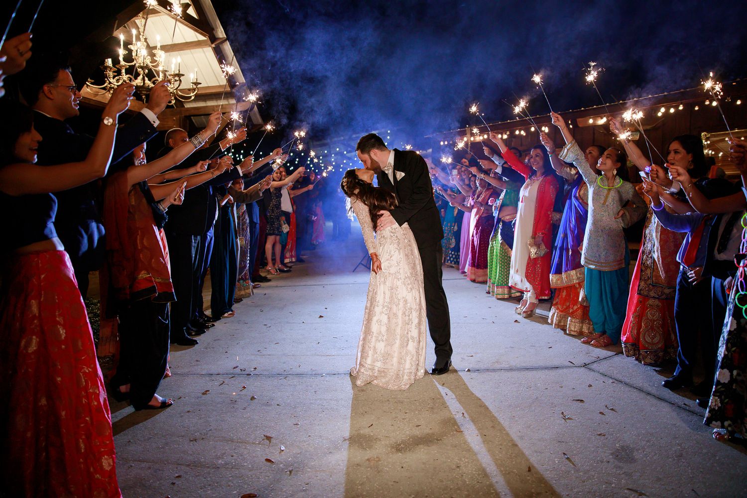 Wedding celebration with sparkler exit as guests line pathway creating magical nighttime moment.